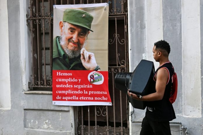 Un hombre que carga con un televisor pasa frente a un cartel del desaparecido líder cubano Fidel Castro, el 27 de febrero de 2026 en La Habana. AFP