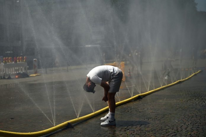 Un hombre se remoja la cabeza con una gran manguera que arroja chorros de agua, instalada en una calle de Colonia para combatir la ola de calor, el 25 de junio de 2026 en esa ciudad al oeste de Alemania. AFP