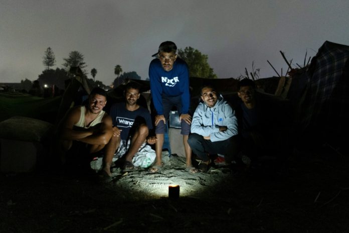 Un grupo de migrantes posa para la foto iluminados con la linterna de un teléfono móvil, el 1 de septiembre de 2026 en la playa de El Trampolín de Ceuta, ciudad española al norte de África. AFP