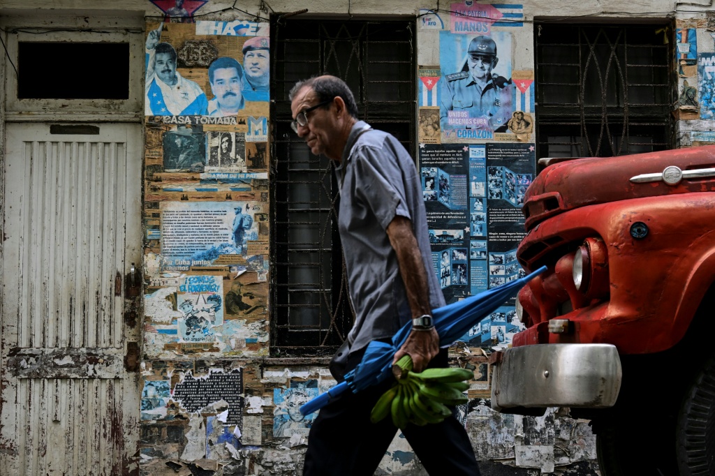 Un hombre camina frente a carteles de Raúl Castro, Nicolás Maduro y Hugo Chávez en La Habana