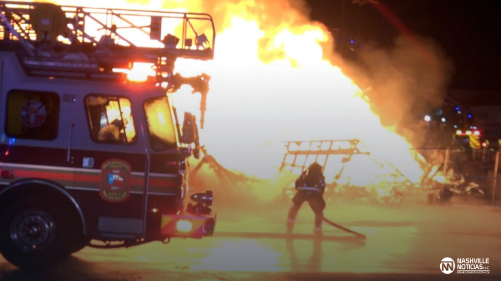 Camión de bomberos y un bombero frente a un gran incendio durante la noche