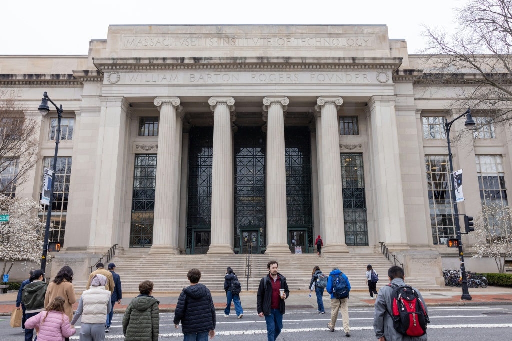 Universidades de EE. UU.: estudiantes cruzan una calle frente a un edificio del MIT en Cambridge, Massachusetts