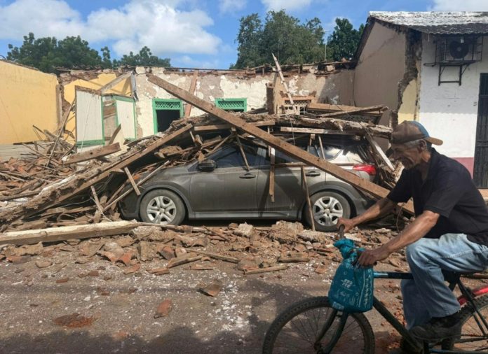 Un hombre monta en bicicleta frente a una casa derrumbada y un automóvil enterrado bajo los escombros en la ciudad de Chitré, a unos 250 km al suroeste de Ciudad de Panamá, el 10 de octubre de 2026. AFP